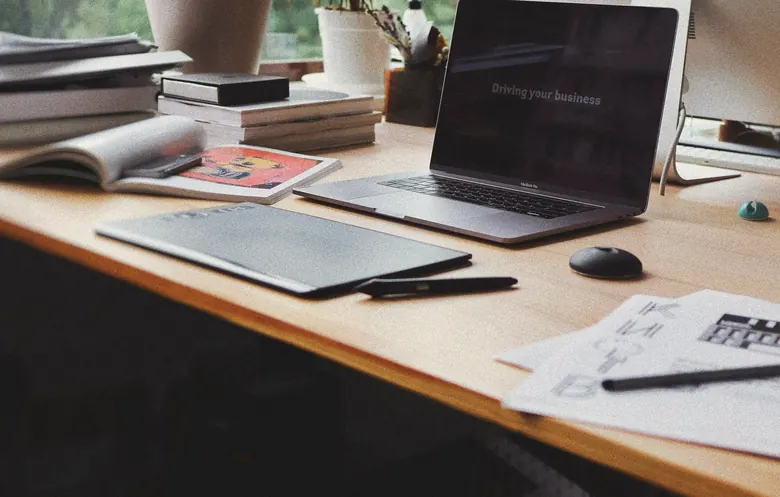A calm wooden desk by a window with a laptop, notebooks and plants